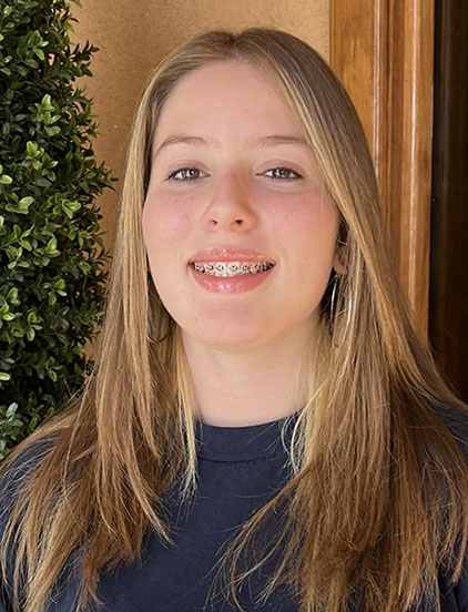 Young woman smiling at camera in professional office setting with greenery background.