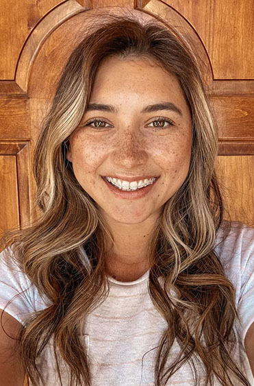 Smiling woman with long wavy hair against wooden background, wearing white t-shirt.