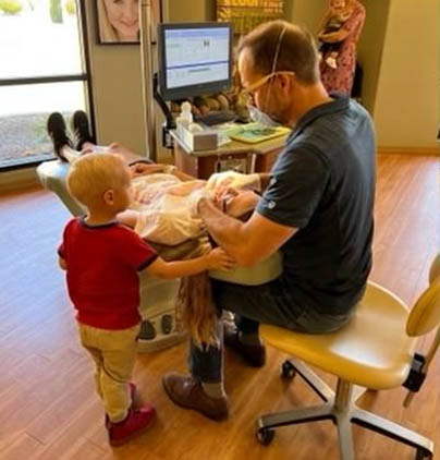 Adult and toddler playing with toys in a bright, welcoming orthodontic office reception area.
