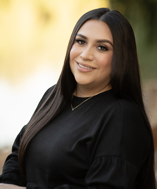 Young woman smiling at camera wearing black shirt in outdoor portrait setting.